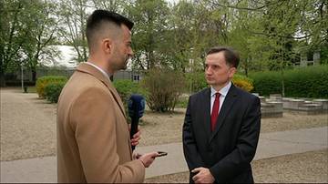 Zbigniew Ziobro w garniturze i z czerwonym krawatem stoi na zewnątrz i rozmawia z dziennikarzem trzymającym mikrofon z logo Polsat News.