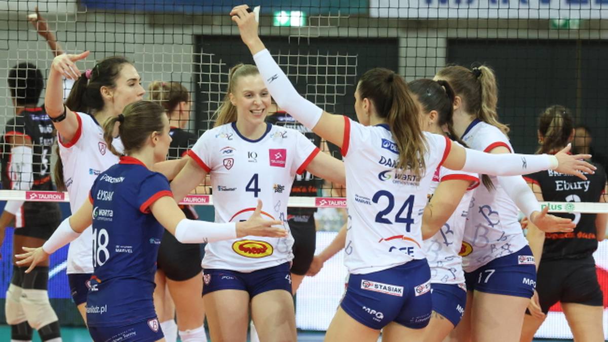 Siatkarki w białych strojach świętują, jedna z nich z numerem 4 uśmiecha się.