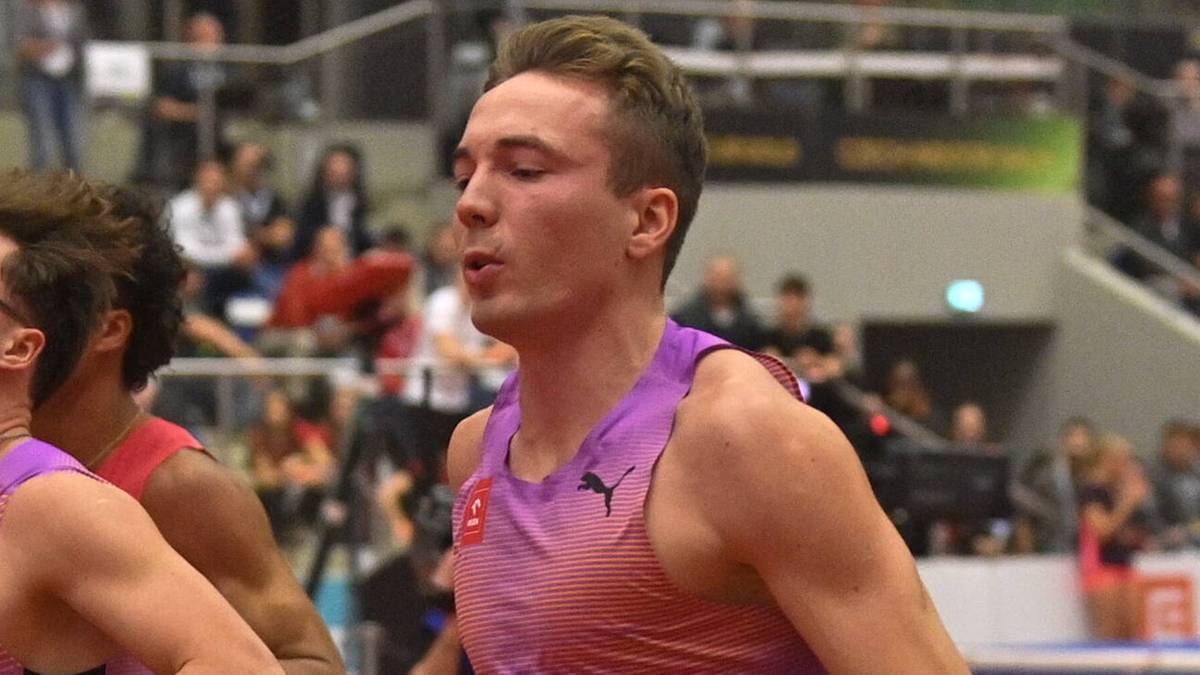 Czterech lekkoatlet&oacute;w w biegu na kr&oacute;tkim dystansie, z widoczną publicznością na trybunach.