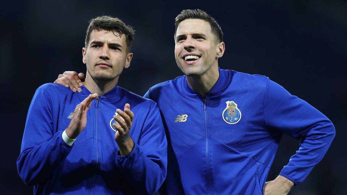 Dwóch piłkarzy w niebieskich strojach sportowych z herbem klubu na piersi. Jeden z nich jest uśmiechnięty, drugi patrzy w bok.