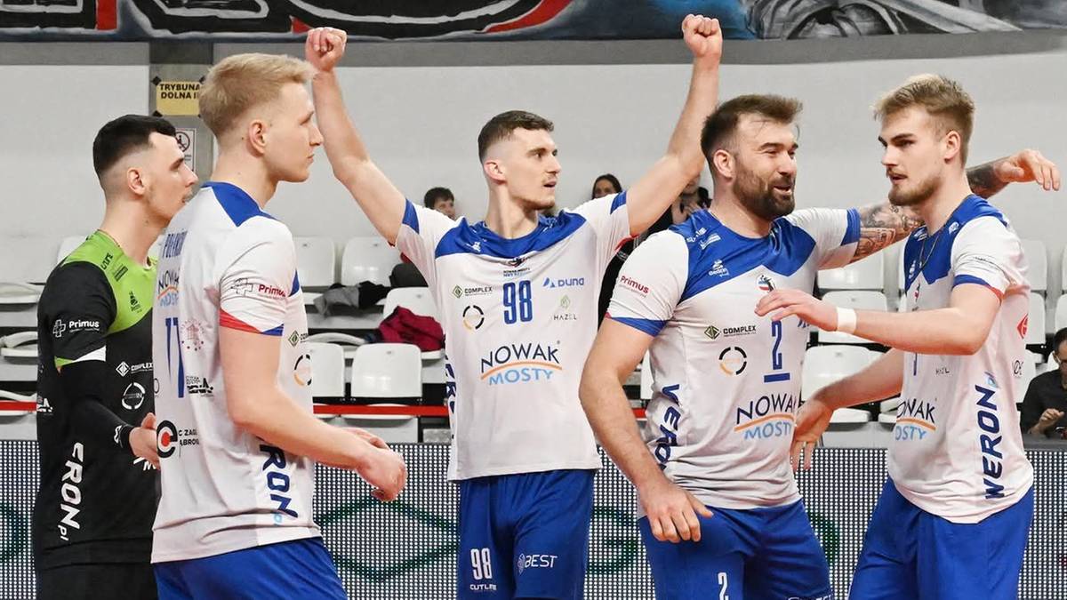 Siatkarze w białych i niebieskich strojach sportowych świętują na boisku siatkarskim.