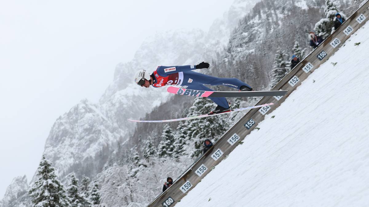Skoczek narciarski w trakcie lotu na tle zaśnieżonych gór.