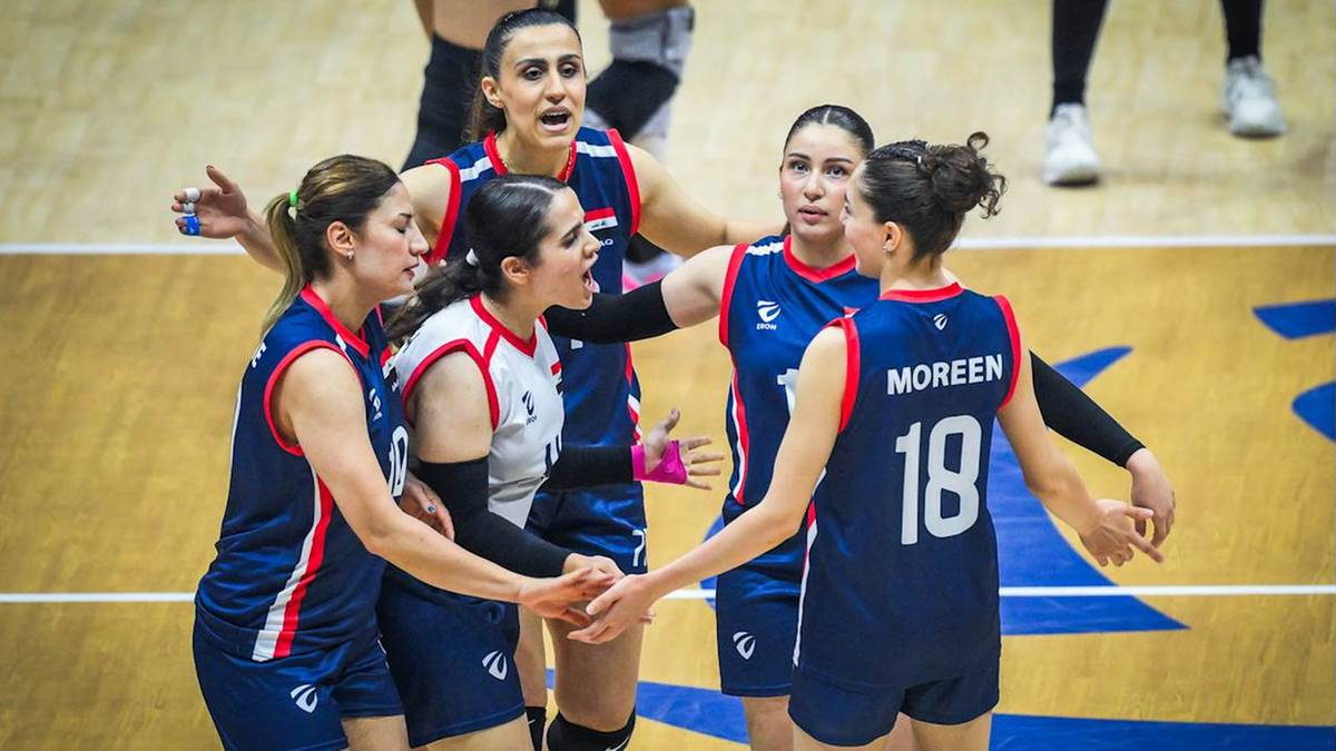 Grupa siatkarek w granatowych strojach sportowych celebruje coś razem na boisku do siatk&oacute;wki.