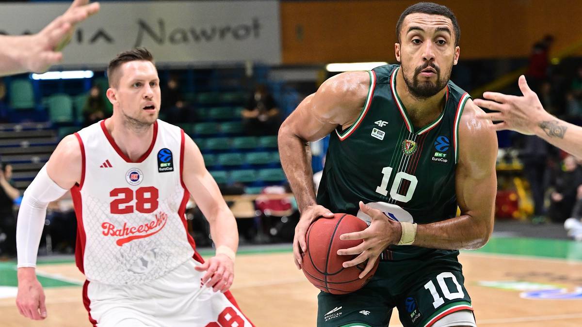 Dw&oacute;ch koszykarzy podczas meczu, jeden w białej koszulce z numerem 28, drugi w zielonej z numerem 10.