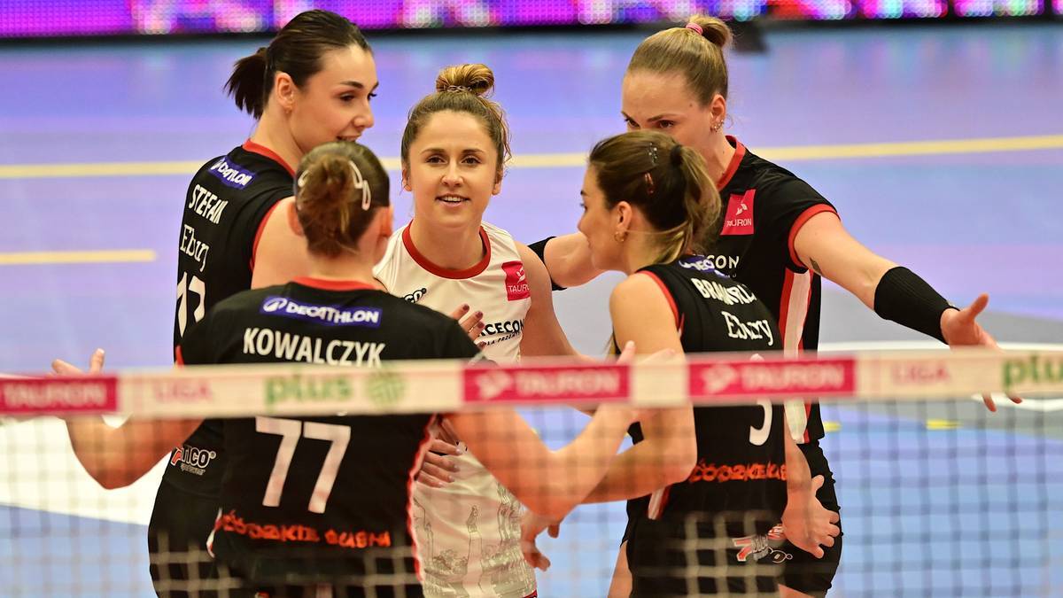 Pięć siatkarek w czarnych i białych strojach sportowych podczas meczu, rozmawiają ze sobą.