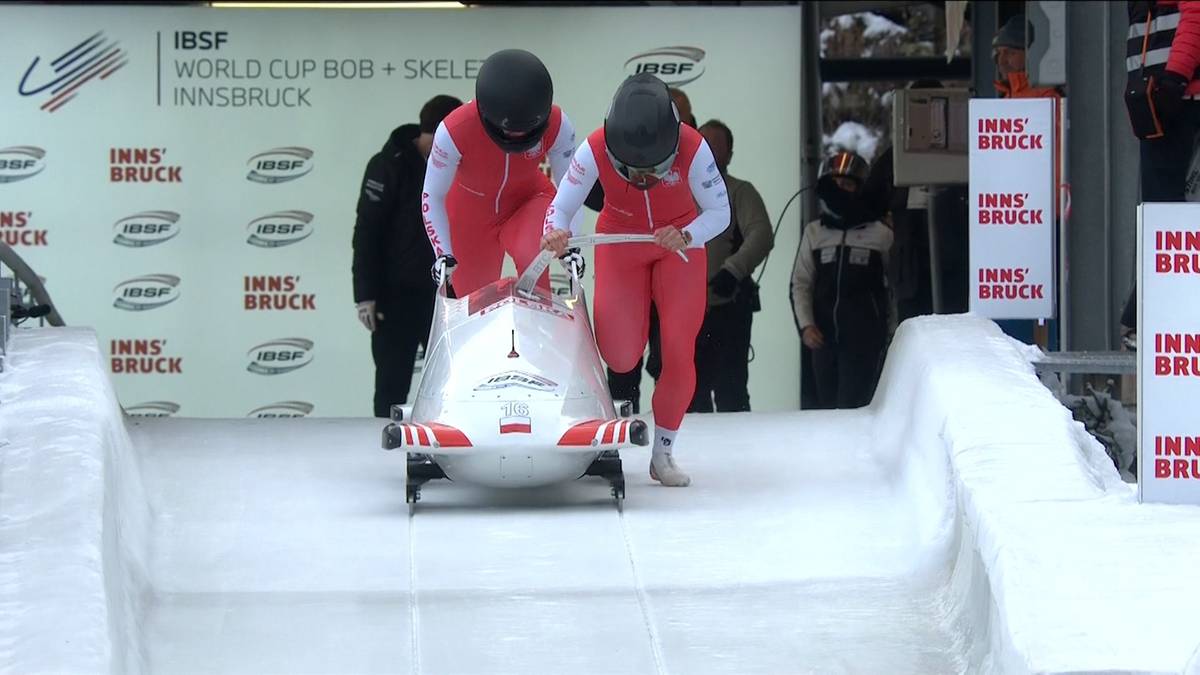 Zawodniczki w czerwono-białych strojach pchają bobslej na lodowym torze.