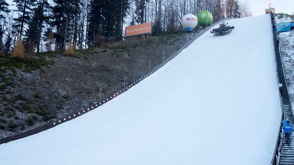 Skocznia narciarska z białą nawierzchnią, na szczycie widoczni ludzie i dwa balony.