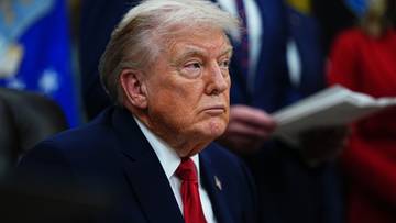 Prezydent USA Donald Trump siedzi w garniturze i czerwonym krawacie, patrząc w bok z poważnym wyrazem twarzy.
