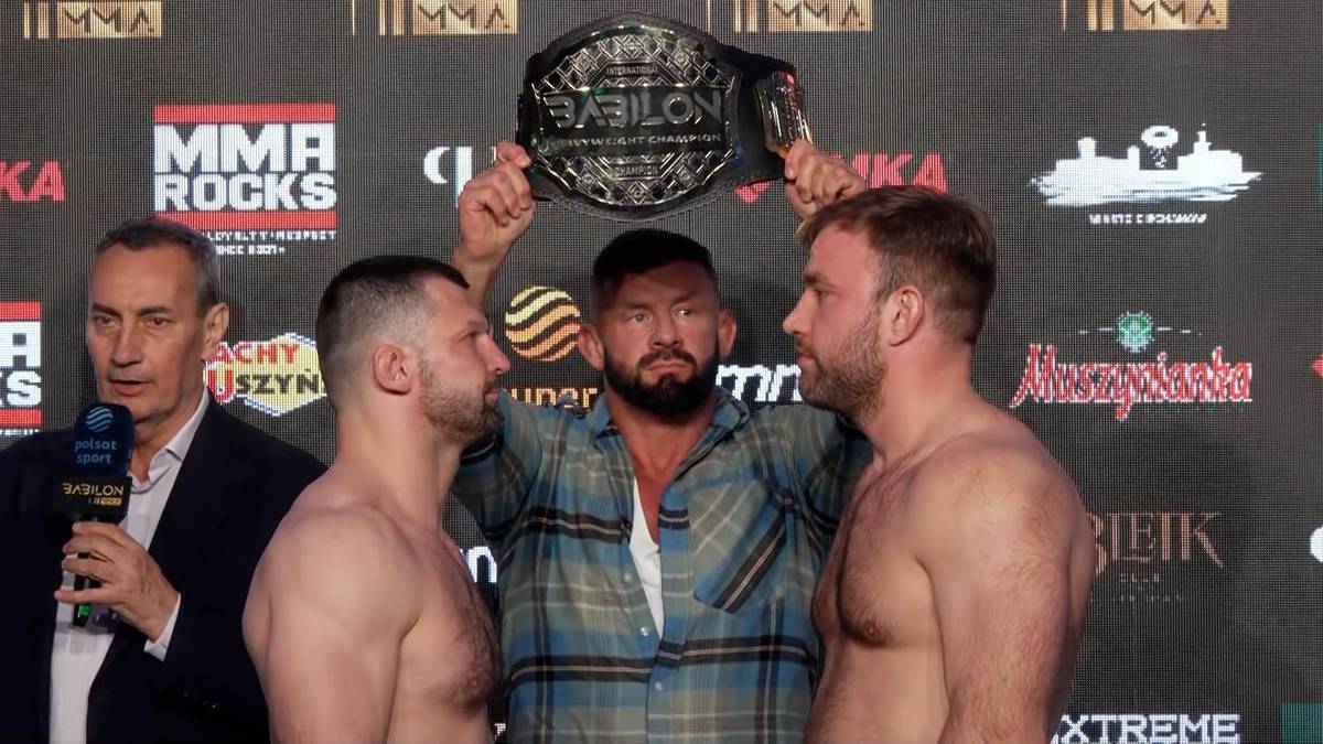 Dw&oacute;ch zawodnik&oacute;w MMA stoi naprzeciw siebie podczas ważenia, a pomiędzy nimi arbiter trzyma pas mistrzowski Babilon MMA nad ich głowami.