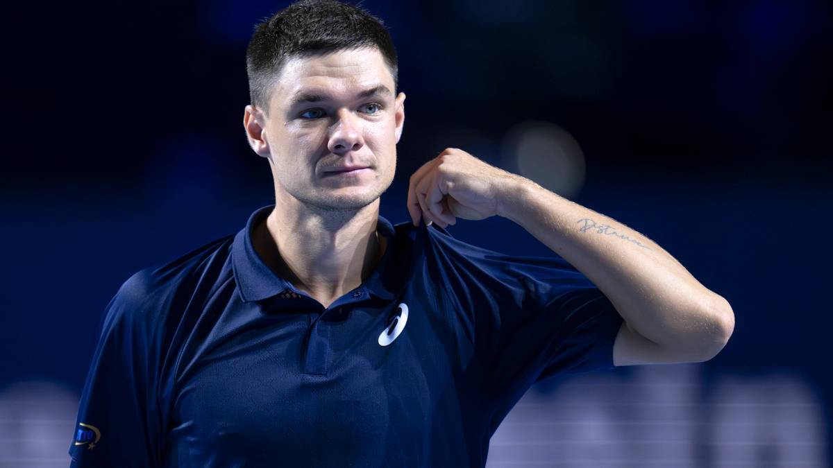 Tenisista Jannik Sinner w ciemnym stroju sportowym na tle niebieskiego oświetlenia