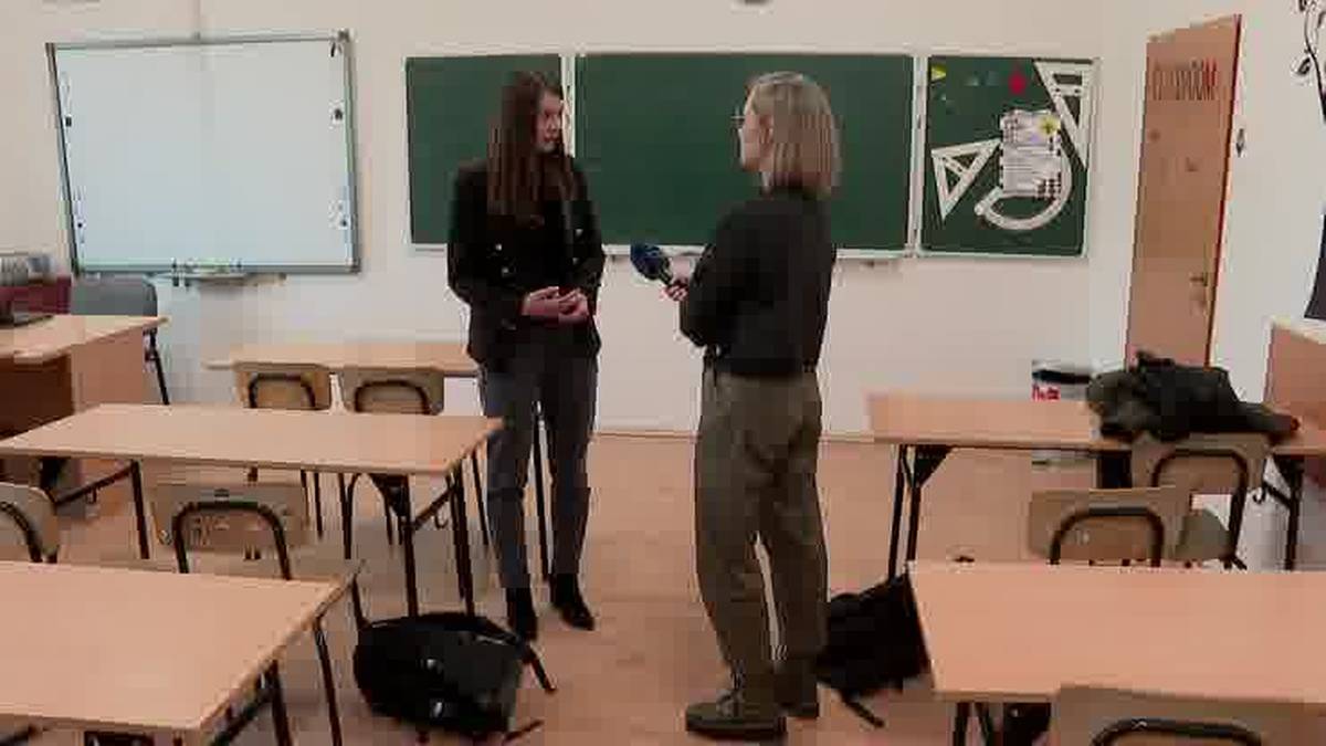 Dwie młode kobiety rozmawiają w sali lekcyjnej. Jedna z nich trzyma mikrofon.