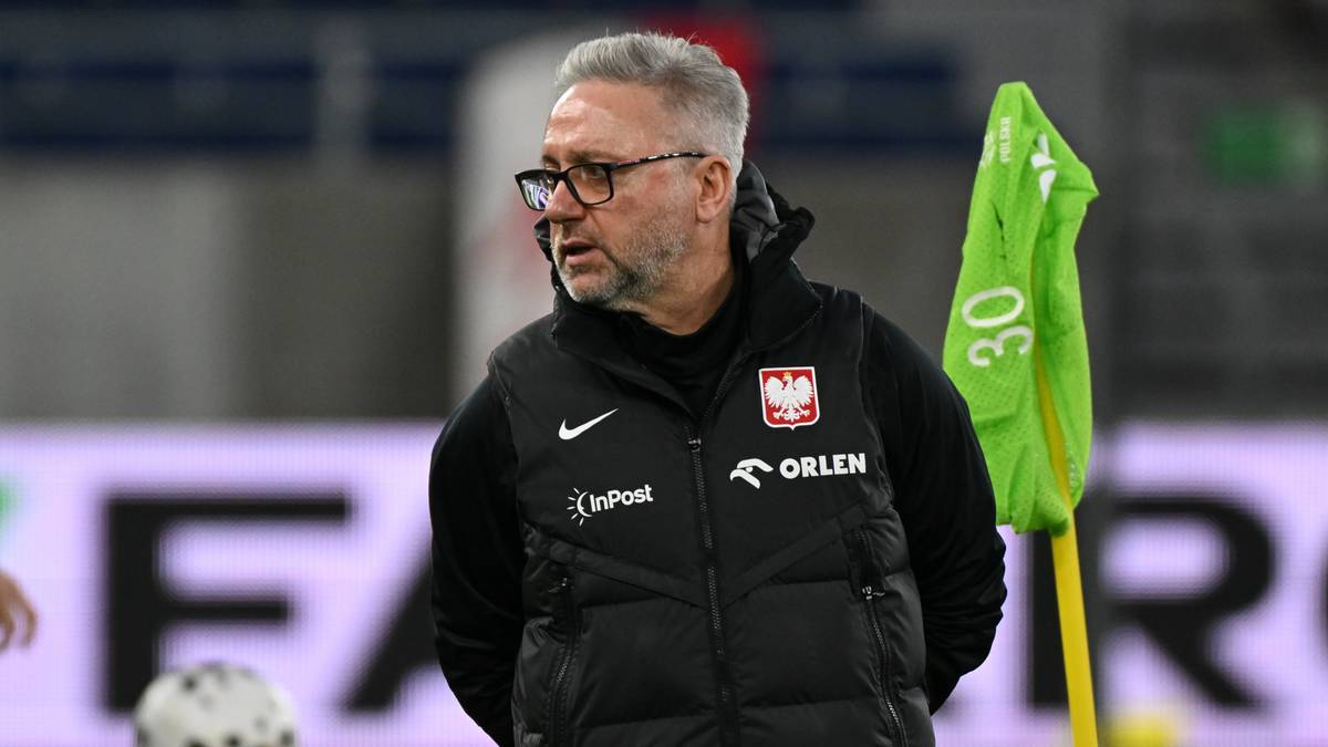 Jerzy Brzęczek, selekcjoner reprezentacji Polski U-21, w okularach i kamizelce, stoi na tle stadionu.