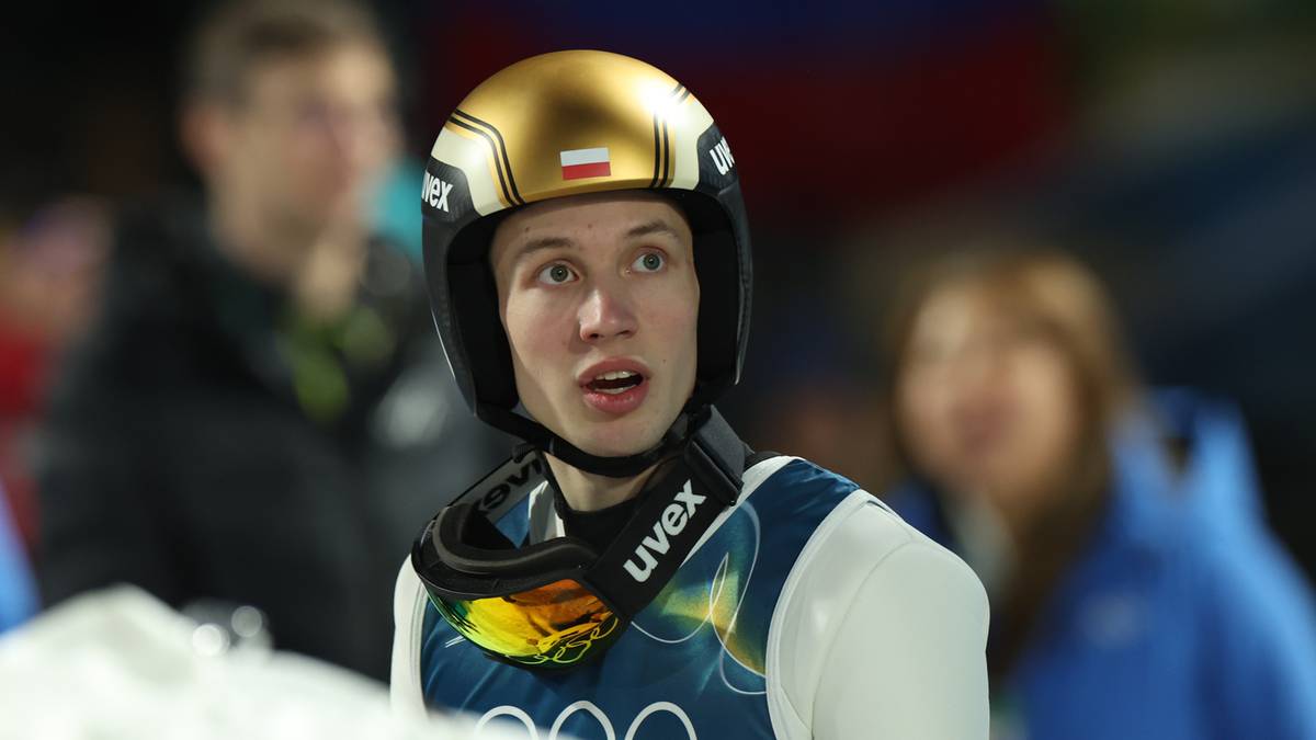 Młody skoczek narciarski w złotym kasku i goglach, z widocznymi innymi osobami w tle.