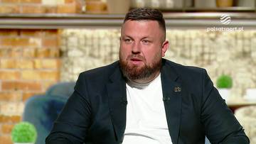 Łukasz Milik, ubrany w ciemną marynarkę i białą koszulkę, siedzi i udziela wywiadu.