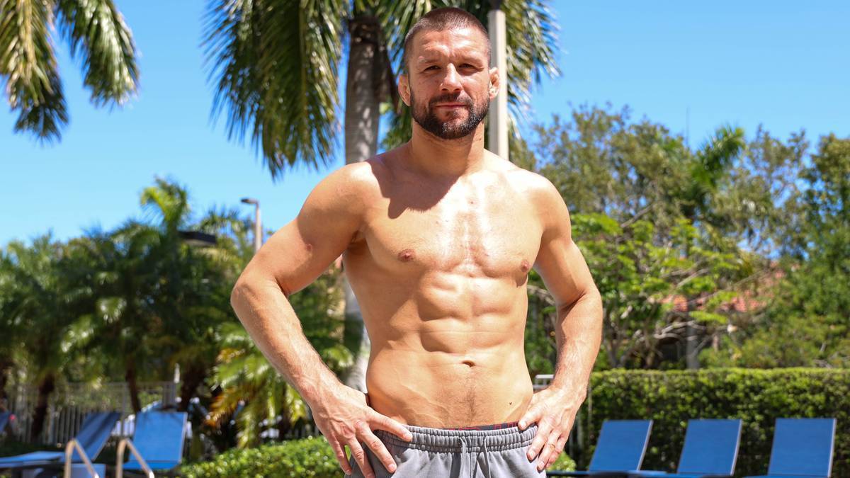 Mateusz Gamrot, umięśniony mężczyzna bez koszulki, stoi na zewnątrz, patrząc w obiektyw.
