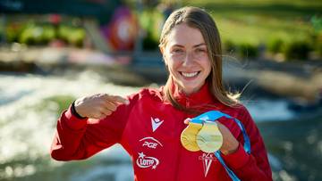 Uśmiechnięta kobieta w czerwonej bluzie sportowej z medalami na szyi.