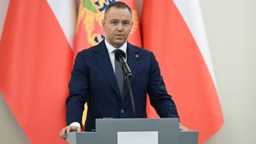 Mężczyzna w garniturze przemawia za m&oacute;wnicą na tle flag Polski i Montenegro.