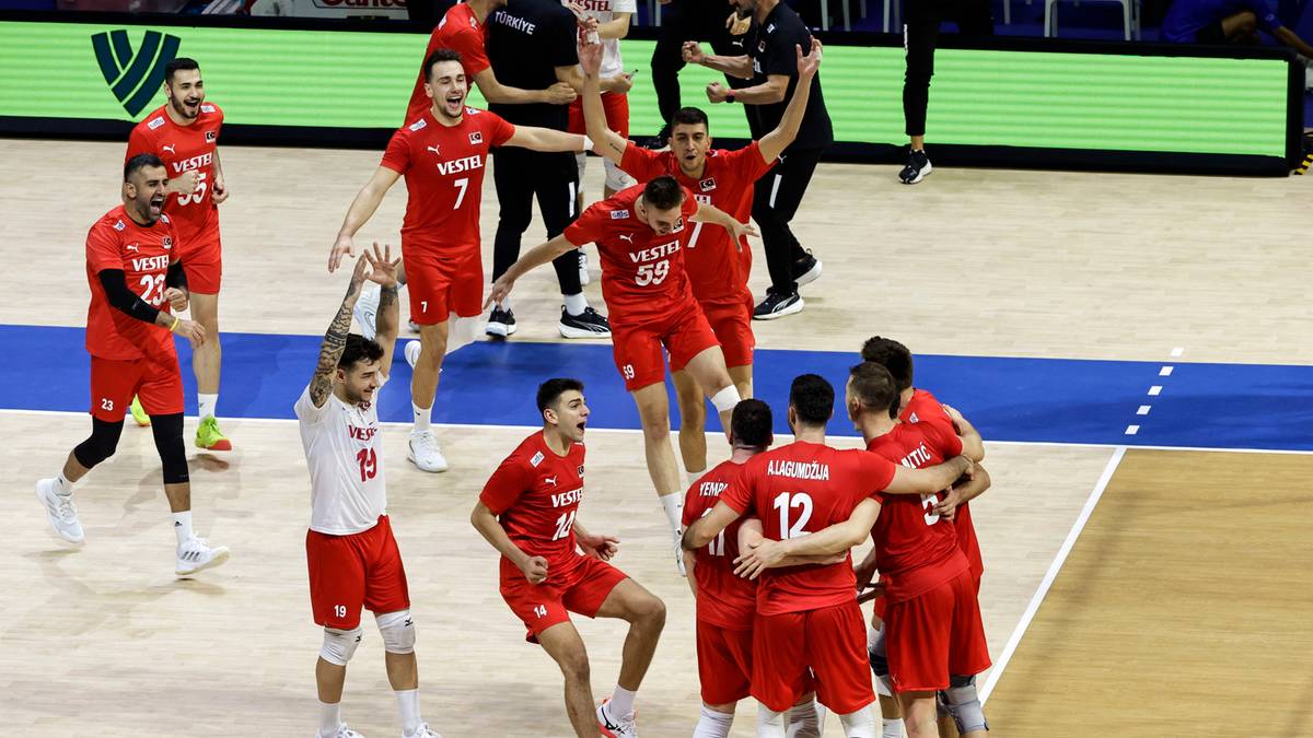 Drużyna siatkarzy w czerwonych strojach radośnie świętuje zwycięstwo na boisku, przytulając się.