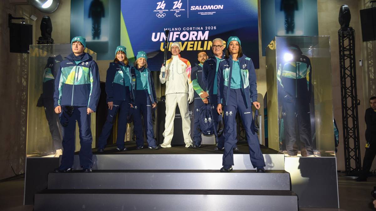 Osoby w strojach sportowych prezentują nowe uniformy na scenie z logo igrzysk olimpijskich.