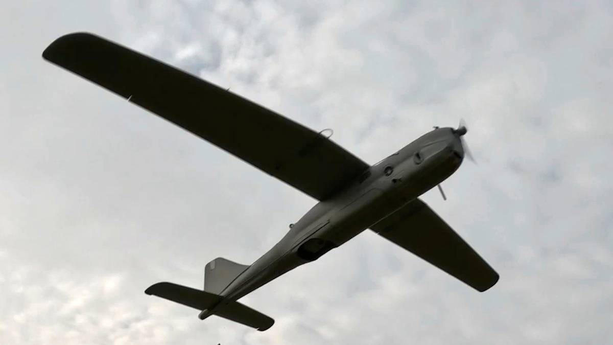 Dron zwiadowczy w locie nad polem, obok niego wyrzutnia z obsługą.