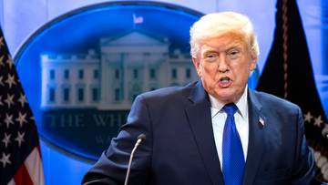 Donald Trump przemawia przed symbolami Białego Domu i flagami USA.