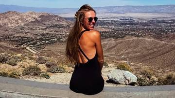 Kobieta w czarnej sukience siedząca na murku z widokiem na miasto i g&oacute;ry w tle.