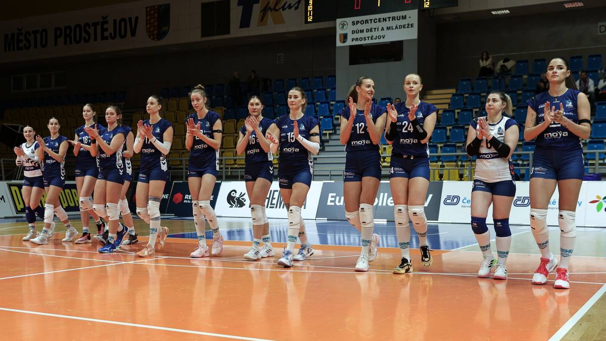 Siatkarki w niebiesko-białych strojach stoją w rzędzie na boisku i klaszczą.