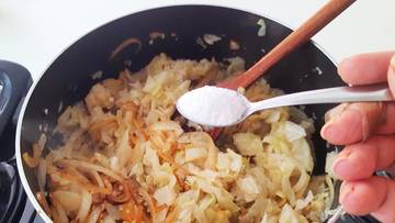 Zbliżenie na garnek z gotującą się kapustą, do kt&oacute;rej z łyżeczki dodawana jest s&oacute;l.