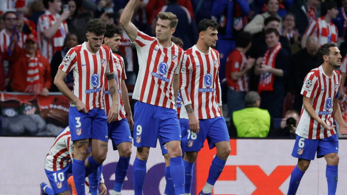 Piłkarze Atletico Madryt w biało-czerwonych koszulkach świętują bramkę, jeden z zawodnik&oacute;w unosi rękę w geście radości.