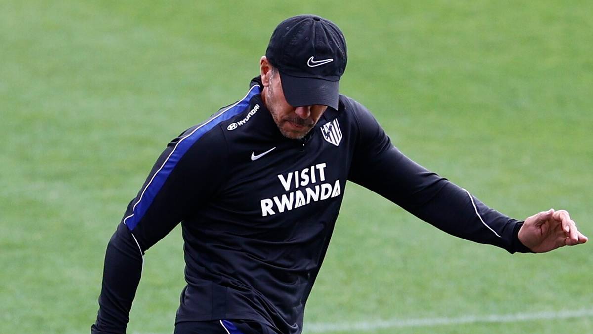 Mężczyzna w czarnej odzieży sportowej z napisem "VISIT RWANDA" i czapce z logo Nike, na tle zielonej murawy.