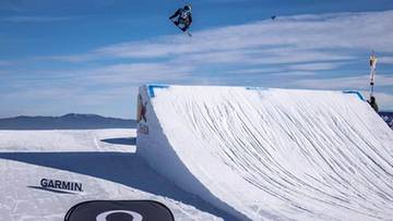 Snowboardzista wykonujący skok w powietrzu nad śnieżną rampą.