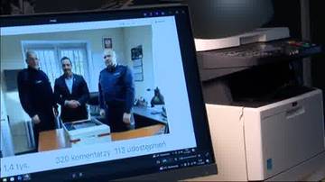 Trzech mężczyzn w policyjnych mundurach stoi przed drukarką, której obraz wyświetlany jest na ekranie komputera.