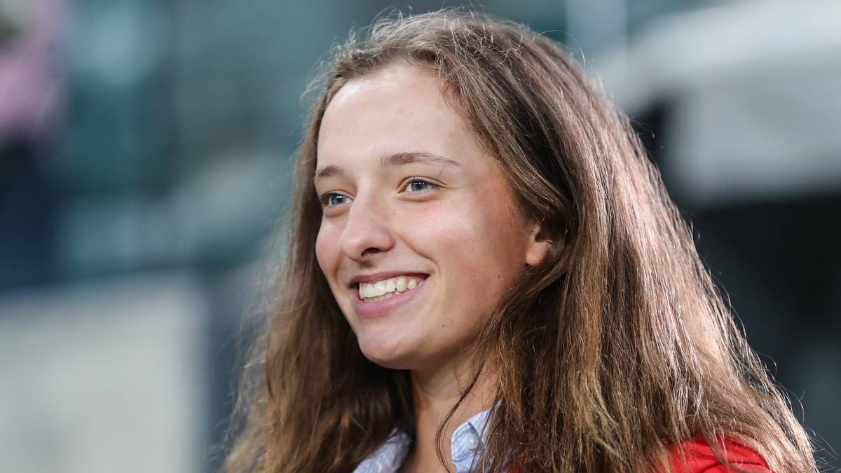 Uśmiechnięta Iga Świątek patrzy w bok, z rozwianymi brązowymi włosami.