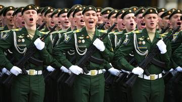 Grupa rosyjskich żołnierzy w zielonych mundurach i czapkach, trzymających broń, maszeruje w rzędzie.