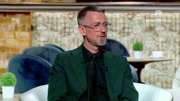 Mężczyzna w okularach i zielonej marynarce siedzi w studiu telewizyjnym, prawdopodobnie podczas programu "Cafe Futbol".