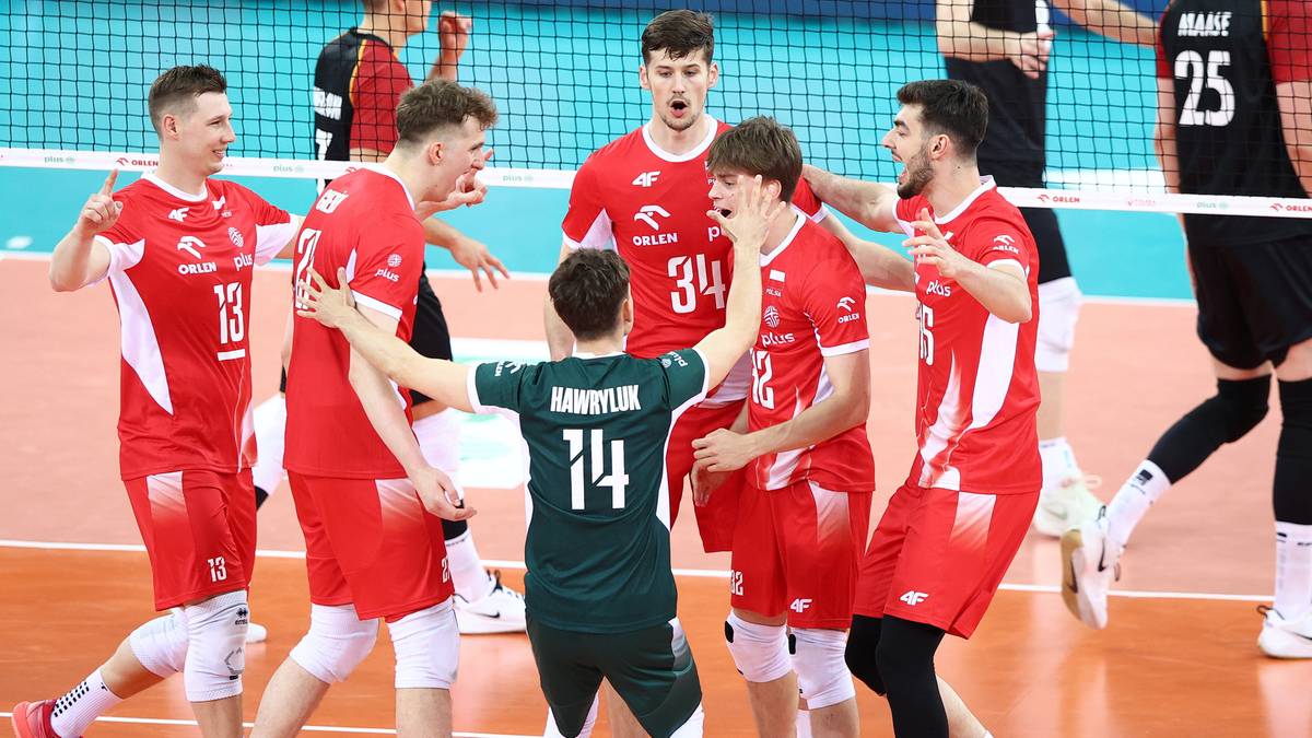 Grupa mężczyzn w czerwonych strojach siatkarskich cieszy się po meczu, jeden z nich w zielonym stroju jest otoczony przez pozostałych.