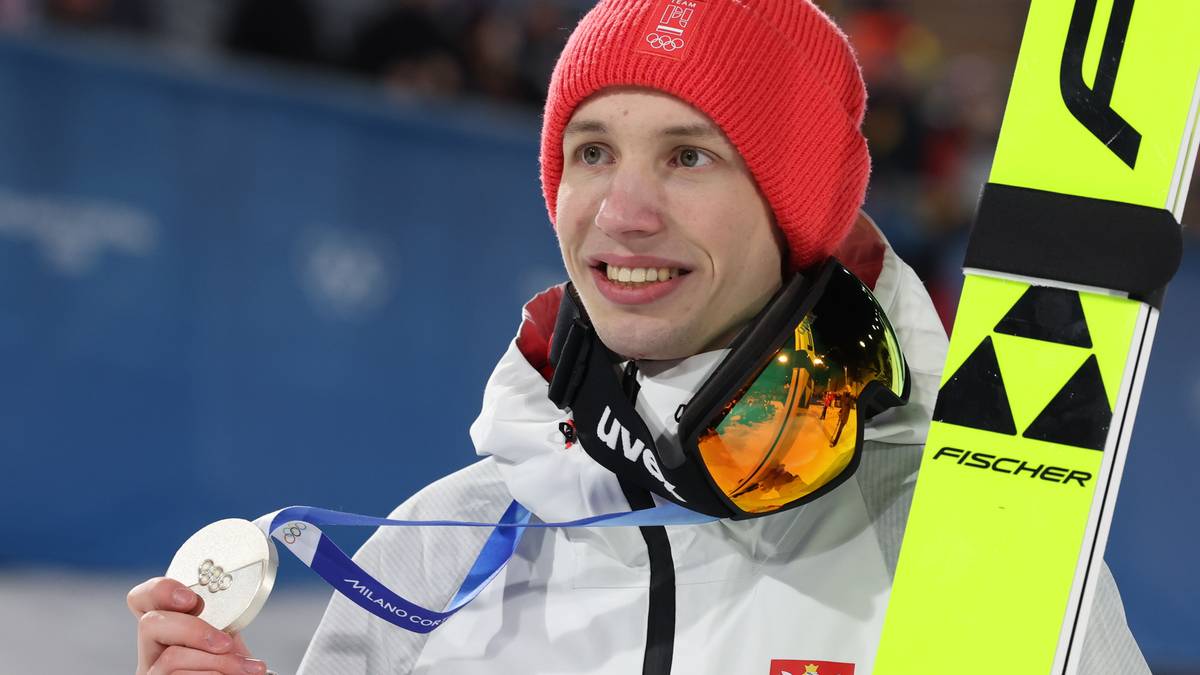 Skoczek narciarski w czerwonej czapce trzyma medal i narty.