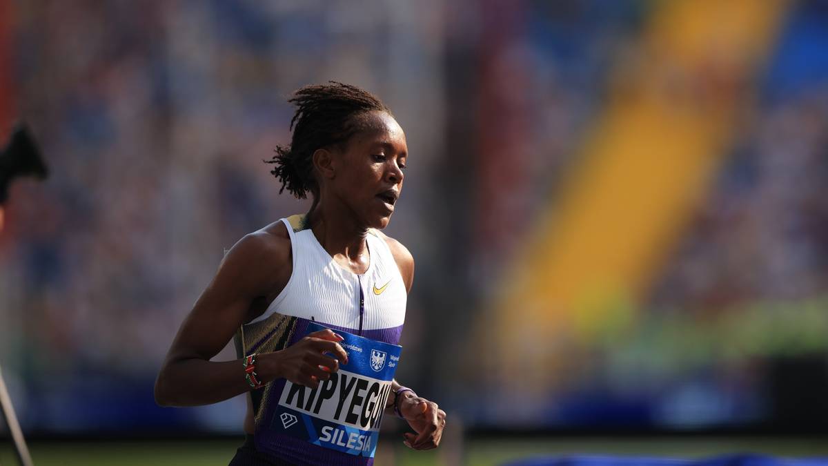 Atletka Kenijka w białej koszulce z niebieskimi napisami biegnie podczas zawodów.