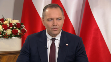 Prezydent Karol Nawrocki w garniturze i krawacie, na tle flag Polski.