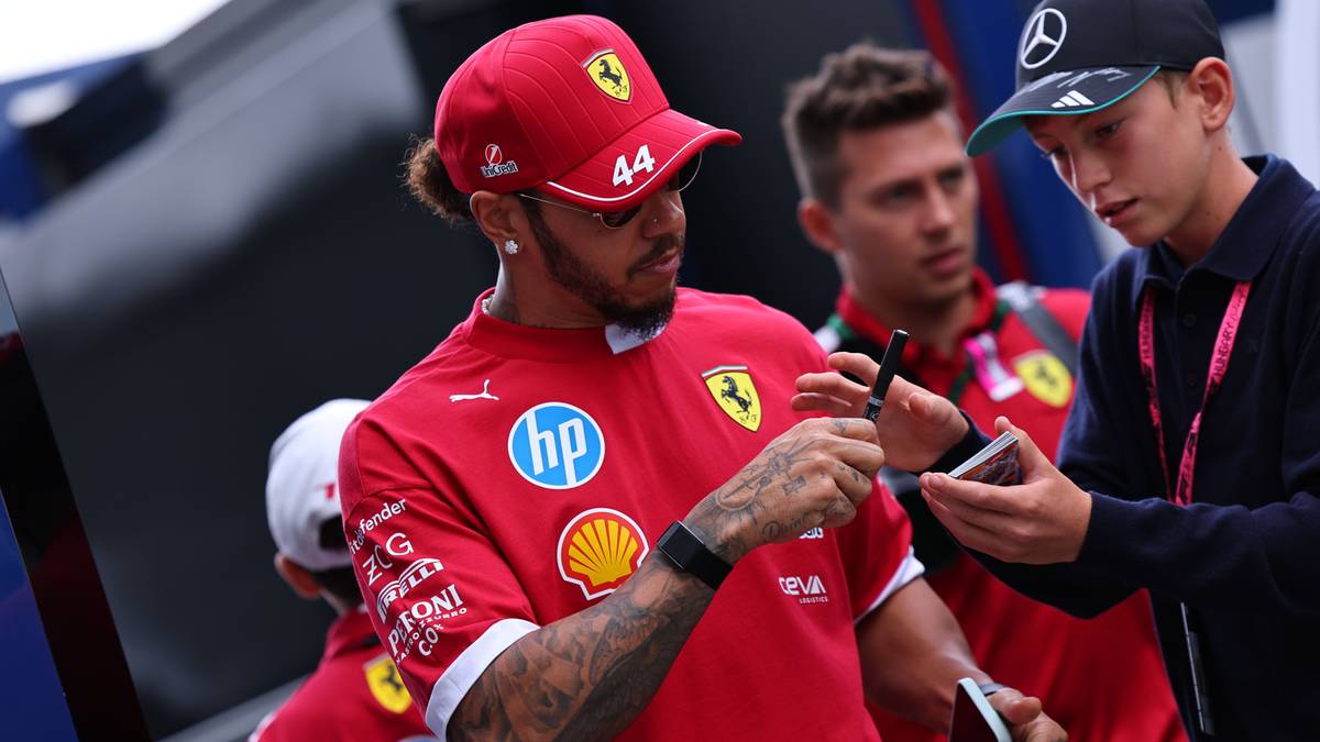 Lewis Hamilton w czerwonym stroju zespołu Ferrari trzyma telefon i długopis.