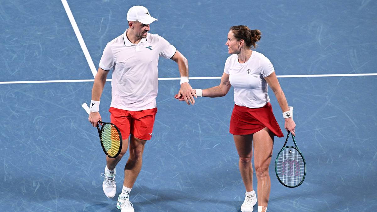 Para tenisistów w strojach sportowych, mężczyzna i kobieta, trzymają się za ręce na korcie tenisowym, oboje uśmiechnięci.