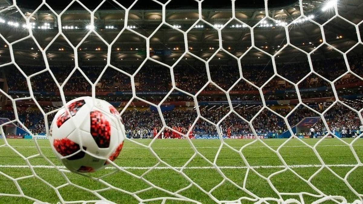 Piłka do piłki nożnej w siatce bramki na tle stadionu.