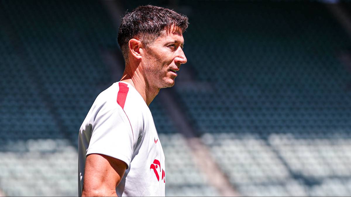 Robert Lewandowski w białej koszulce na tle stadionu.