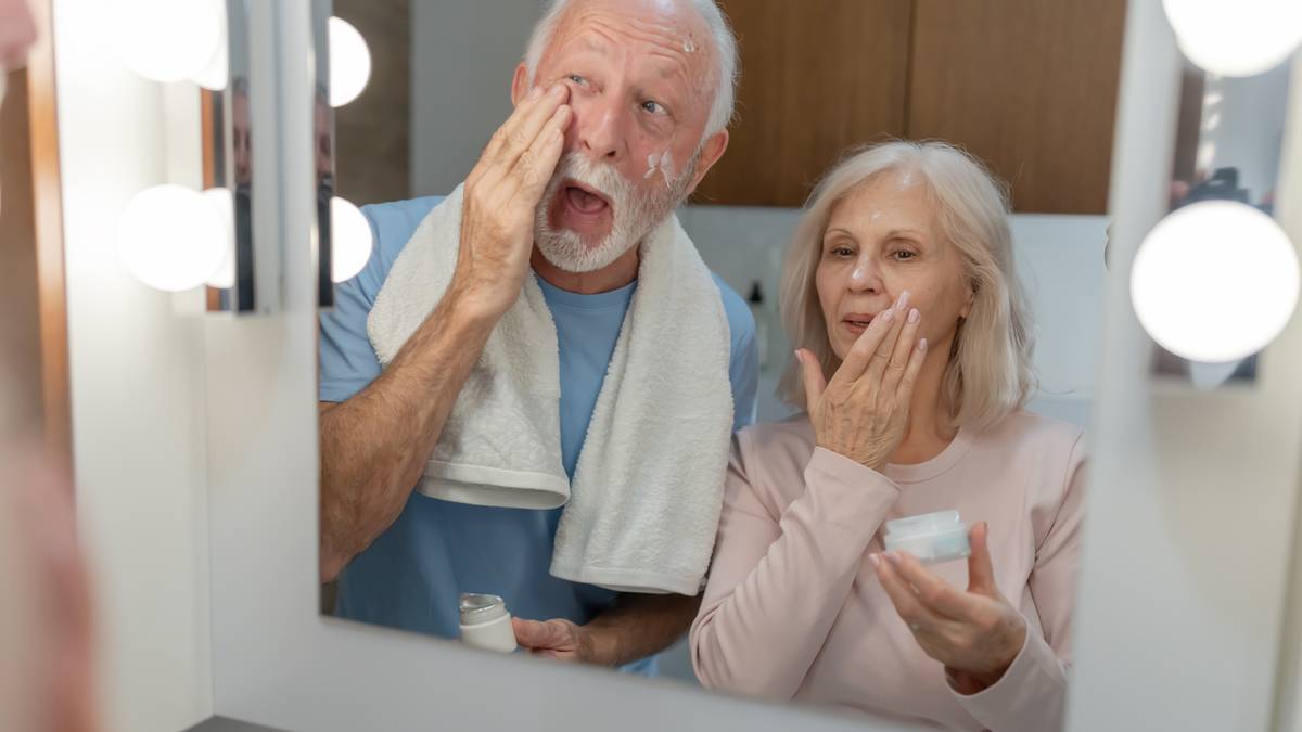 Starsza para aplikująca krem do twarzy przed lustrem.