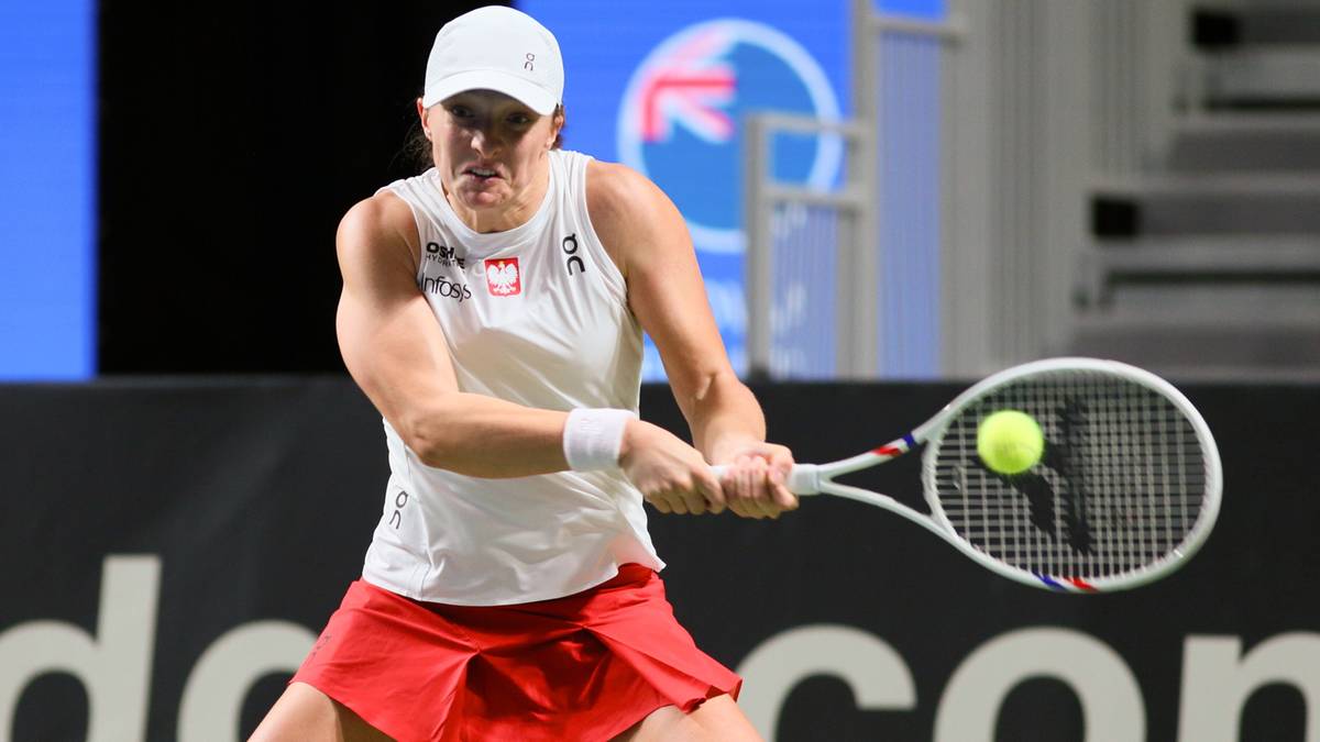 Tenisistka w białej czapce i stroju z czerwonymi spodenkami, trzymająca rakietę tenisową i uderzająca piłkę.