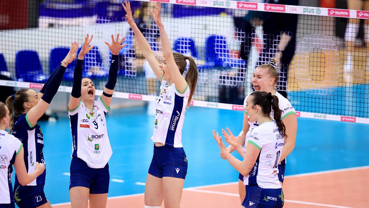 Siatkarki w białych i granatowych strojach sportowych cieszą się z punktu, podnosząc ręce do g&oacute;ry.