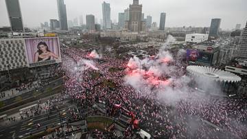 Widok z góry na duży tłum ludzi na placu miejskim, wśród których odpalono czerwone race. W tle widoczne budynki miejskie, w tym Pałac Kultury i Nauki.