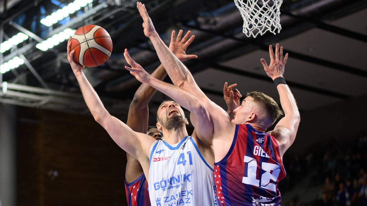 Dw&oacute;ch zawodnik&oacute;w koszyk&oacute;wki walczy o piłkę pod koszem, jeden z nich pr&oacute;buje oddać rzut.
