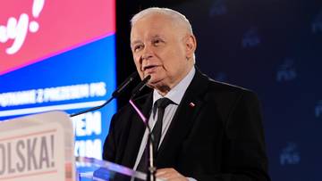 Starszy mężczyzna w garniturze przemawia przy mównicy na tle ekranu z napisem "Dziękujemy!".