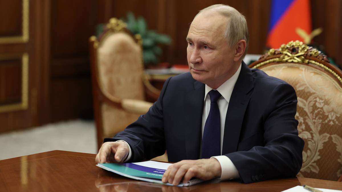 Władimir Putin siedzi przy stole w garniturze i krawacie, z rękami opartymi na dokumentach.